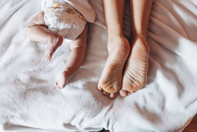 Top view of crop newborn baby in diaper lying on bed with mother in house