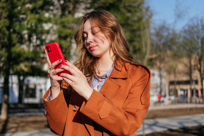 Smiling young woman using smartphone outdoors. girl looking at mobile phone in park.