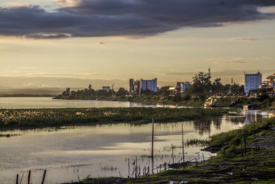 Scenic view of lake by buildings against sky at sunset