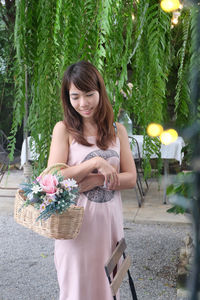 Smiling young woman standing by flower plants