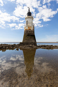 Lighthouse by sea against sky