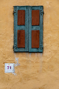 Wooden window in brown and indigo colors on ocher wall at number 71