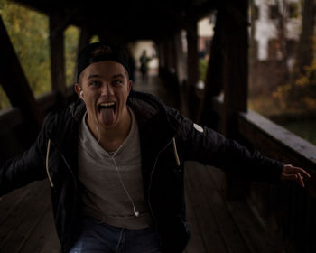 Portrait of young man making face while standing on bridge