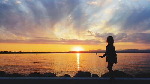 Silhouette girl looking at sea against sky during sunset