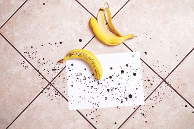 High angle view of banana with ink spots and paper on tiled floor
