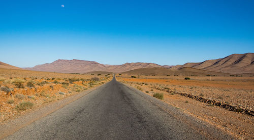 Road amidst desert against clear blue sky