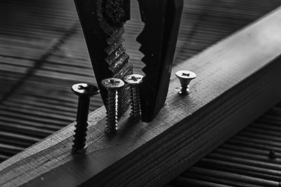 Close-up of pliers removing screws on wood at table