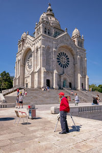 People walking in front of historic building against sky