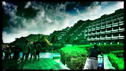 People walking on grassy field against cloudy sky