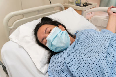 High angle view of woman wearing mask sleeping on bed in hospital