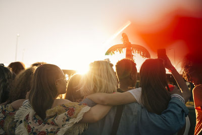 Rear view of friends enjoying music festival against sky in summer