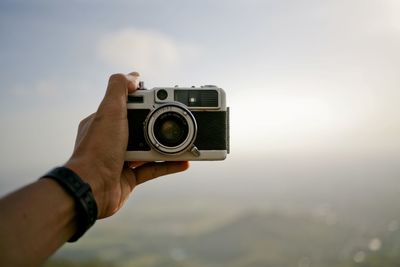 Cropped hand holding camera against sky