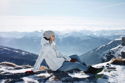 Side view of woman sitting on snowy mountain peak