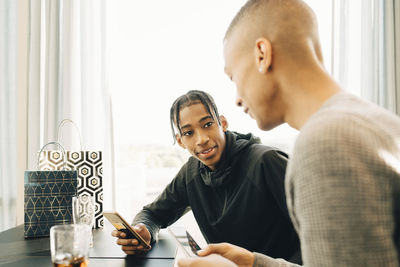 Male friends talking while holding mobile phones in restaurant