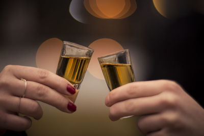 Close-up of hand holding beer glass against black background