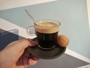 Cropped image of woman hand holding espresso cup with snack against window