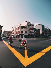 Full length of women riding bicycles on street in city against sky