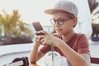 Boy using mobile phone while holding sitting outdoors