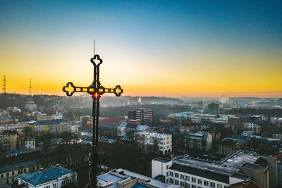 Religious cross overlooking cityscape against clear sky during sunset