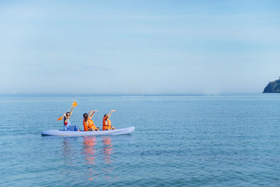 Friends kayaking on sea against blue sky