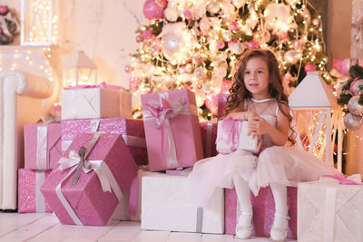 A beatiful girl with curly hair in white dress is holding of christmas box gift and sitting on gift 