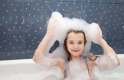 Portrait of smiling girl having bubble bath in bathtub at home