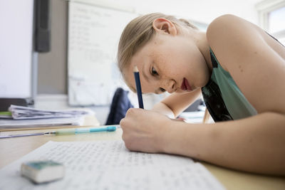 Side view of girl writing in book at classroom