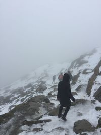 Rear view of friends hiking on snowcapped mountain in foggy weather