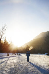 Rear view of man walking on snow covered landscape against clear sky