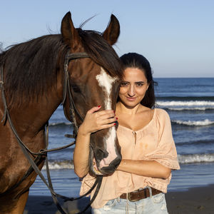 Portrait of smiling young woman with horse standing at beach