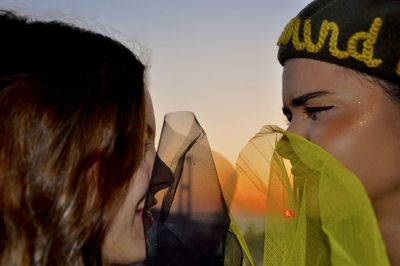 Close-up of friends with scarf against sky during sunset