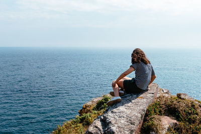 Man sitting on rock by sea against sky