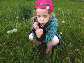 The girl in the grass squatted down. blowing on a dandelion.