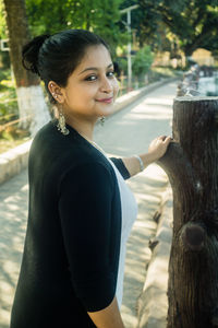 Portrait of smiling woman standing on tree trunk