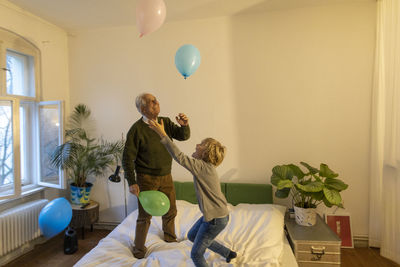 Happy grandfather and grandson playing with balloons on bed at home