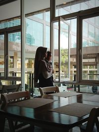 Mother carrying son while looking through window at restaurant