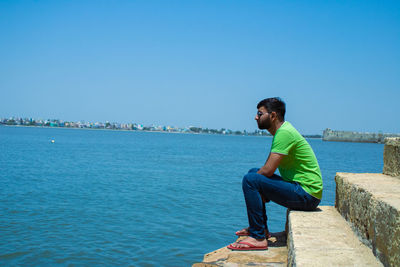 Man sitting in sea against clear blue sky