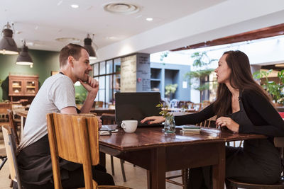 Male and female partners using laptop at table in cafe