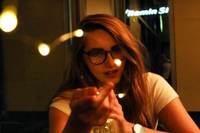 Portrait of young woman gesturing in illuminated restaurant