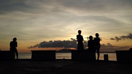Silhouette men standing at beach against sky during sunset