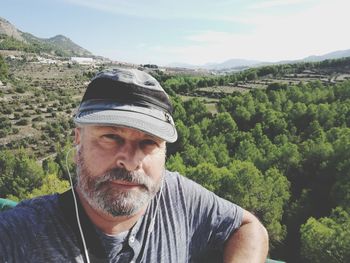 Portrait of man wearing cap listening music against landscape during sunny day