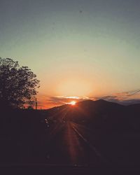 Silhouette trees by road against sky during sunset