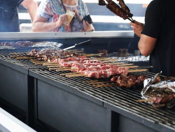 Man holding meat in front of customer by barbecue grill