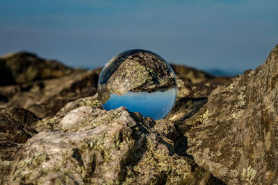 Close-up of glass globe on rock formation on land against sky
