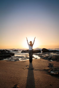 Rear view of young woman exercising on shore at beach during sunset