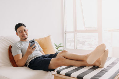 Young woman using mobile phone while lying on bed at home