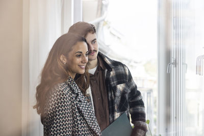 Smiling multiracial couple looking through window in balcony while exploring new house