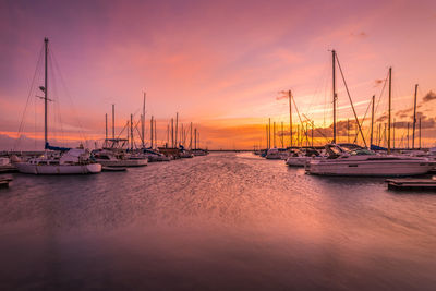 Sailboats moored in marina at sunset