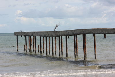 Wooden posts on pier over sea against sky