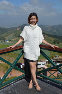 Portrait of smiling woman standing at observation point against sky